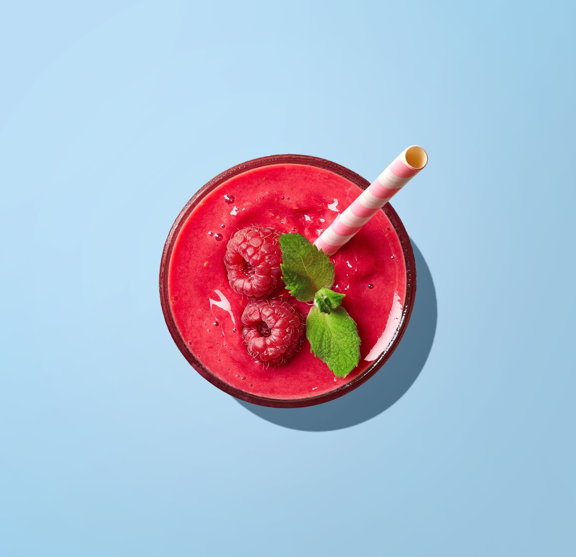 Glass of raspberry smoothie on blue background